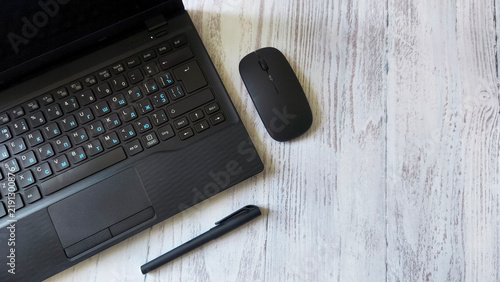 Top view of black laptop, wireless mouse and pen on light wooden table, concept of modern work, productivity, business planning and a minimalist workspace. Copy space