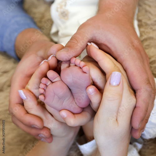 Parents gently hold the tiny feet of a newborn baby, expressing family love, tenderness, care and warmth.