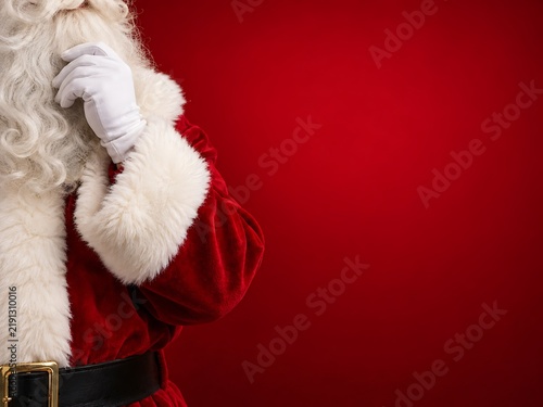 Close up of santa claus touching his white beard wearing a white glove and red suit against a solid vibrant red studio background