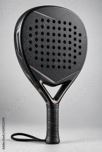 Premium black carbon fiber padel racket displayed vertically on a neutral gray background, showcasing its intricate pattern, perforations, and ergonomic grip for athletic gear.