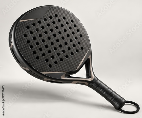 Dynamic angle shot of a sleek black padel racket crafted from carbon fiber, featuring a perforated hitting surface and textured grip, set against a soft gray backdrop.