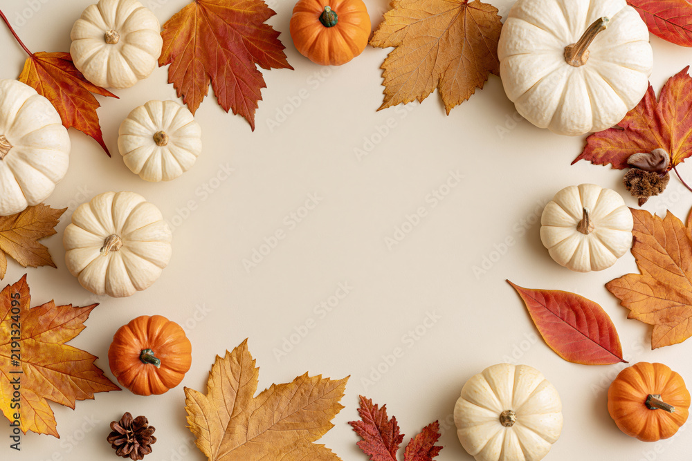Fototapeta premium Autumn pumpkins and fall leaves arranged around a blank cream background for seasonal design