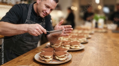 Pastry Chef Carefully Dusting Cocoa Powder Over Heart Shaped Tiramisu Desserts in a Professional Culinary Kitchen Setting
