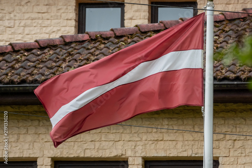 Foto Latvian national flag hanging from a pole beside a tiled building, representing