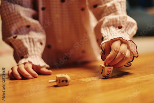 Quadro su tela Child hands playing traditional Hanukkah dreidel game on wooden table at home