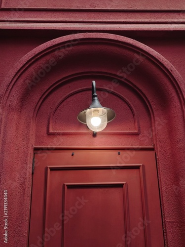 Quadro su tela Glowing vintage style sconce wall lamp mounted above arched red door frame