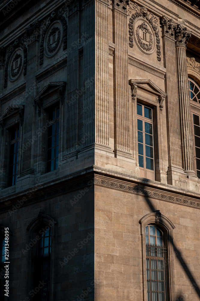 Obraz premium Louvre museum facade in paris, france, showing architectural detail, columns, and windows with sunlight and shadow