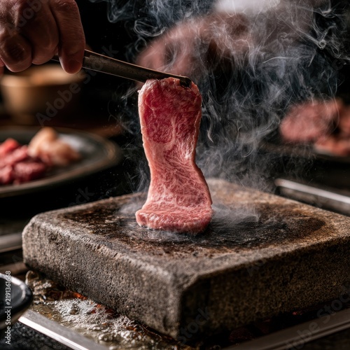 A piece of raw marbled wagyu beef instantly frying on a hot stone grill, smoke, premium dining
