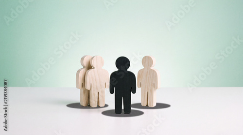 Standing out from the crowd concept with black wooden figure among light wood figures on white surface