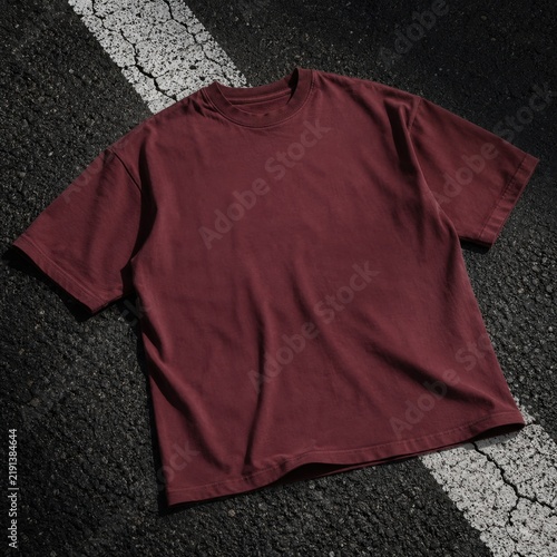 Blank maroon t-shirt mockup, outside pavement background. Short sleeve basic t-shirt laying on asphalt ground. Unisex adult tee, gender neutral casual tshirt mockup