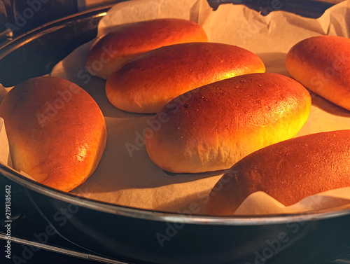 Yeast-dough hand pies baking on a tray in the oven. Traditional russian pastry. Close-up