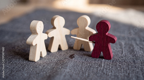 Leadership concept with red wooden figure pointing at group of three natural wood figures on textured surface