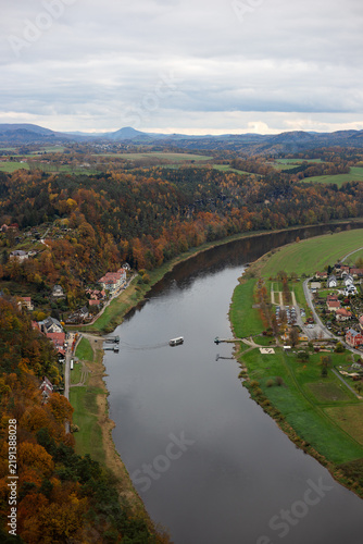Konstfotografi Vertical high-altitude view of the wide Elbe River with a passenger ferry crossing between green banks and autumn forests in Saxon Switzerland