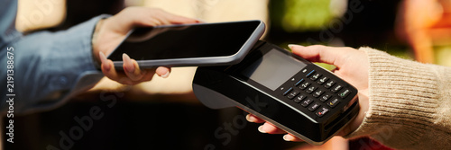 Фотография Header of young woman hands using smartphone for contactless payment via POS terminal machine