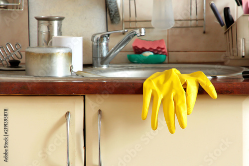 Yellow rubber cleaning glove hanging over a kitchen countertop beside a sink, representing household cleaning, domestic chores, hygiene and everyday home maintenance.