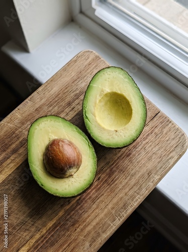 Ripe avocado halves with seed on wooden cutting board