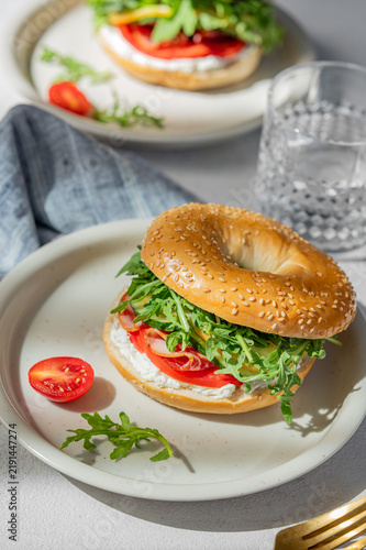 Two fresh bagels with tomato, prosciutto, cheese and arugula on a plates on  a light background
