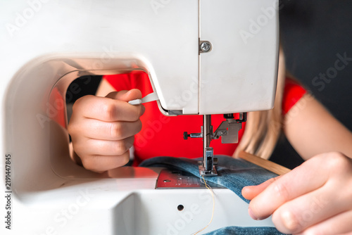 Woman repairing and upcycling jeans with a sewing machine and fabric patch, illustrating circular fashion, visible mending, slow fashion, textile reuse and sustainable DIY.