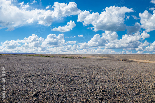Fotografie Vast gravel desert plain under a clear blue sky with white clouds in Xinjiang, C