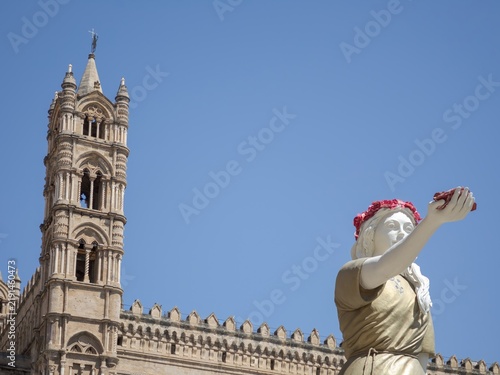 Obraz na plátně Artistic composition capturing the resin statue of Santa Rosalia extending a crown of roses, framed against the stone details of Palermo Cathedral's bell tower