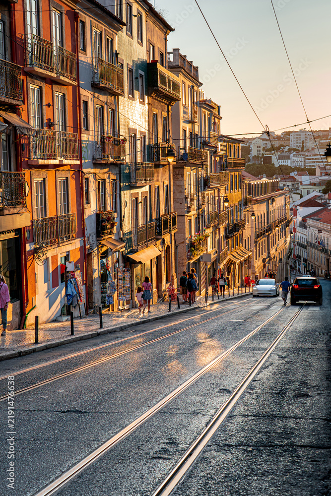Fototapeta premium Vertical photo people walking during golden sunset light in city, Lisbon, life in Portugal, sightseeing, historic architecture.