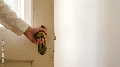 Person hand opening a white wooden door with a vintage brass knob