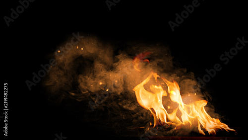 Obraz na płótnie Vibrant fire flames with smoke and glowing sparks against a dark black background, ideal for overlay effects