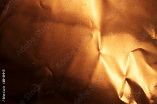 Abstract background of a textured, shiny, and crumpled copper-colored material.