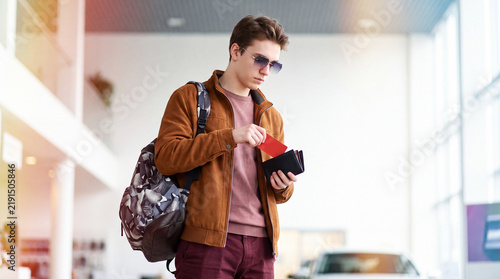 A stylish young man with a backpack takes out a red bank card from his wallet to make purchases at a car dealership. Payment by bank card