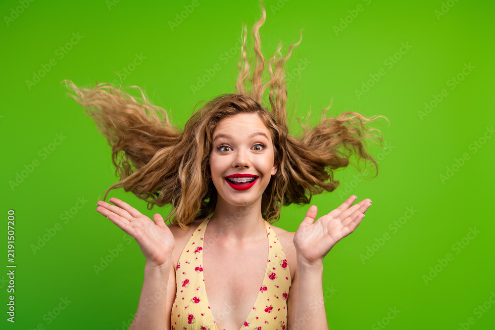 Obraz premium Joyful young woman with blonde hair wearing a floral top poses in front of a vibrant green background
