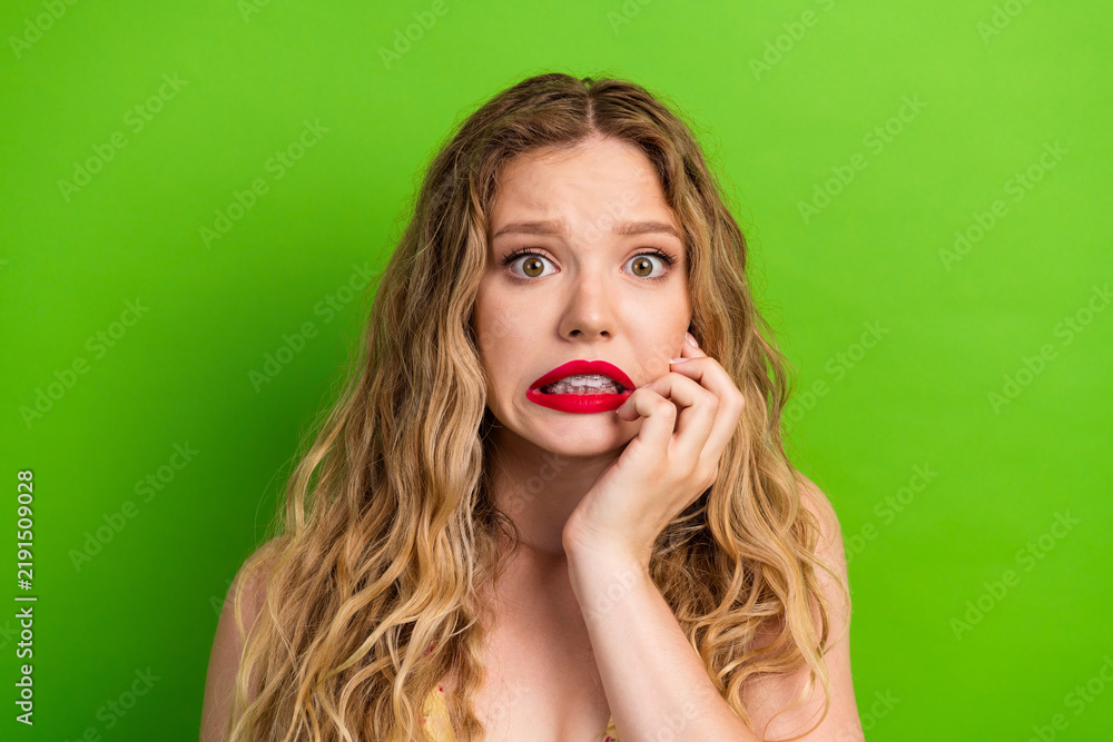 Obraz premium Glamorous young woman with blonde hair biting lip against bright green background