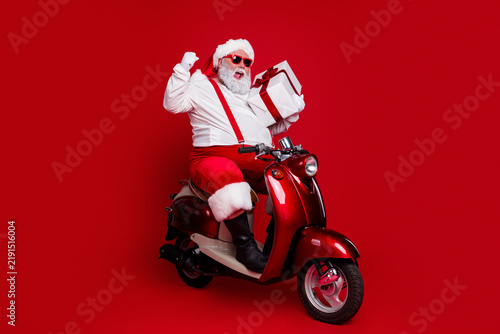 Santa Claus on a red scooter holding a wrapped gift, celebrating Christmas with festive style and playful holiday spirit