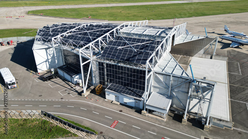 Aerial view of the aircraft engine run-up pen at Geneva Airport, featuring a large metal structure covered with solar panels, tarmac, and parked private jets in Geneve, Switzerland.