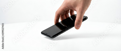 Adult hand picking up black smartphone from white table