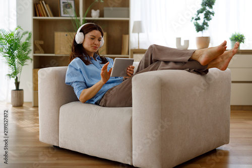 Quadro su tela Woman reclining in a cozy armchair at home, barefoot and relaxed, wearing wirele