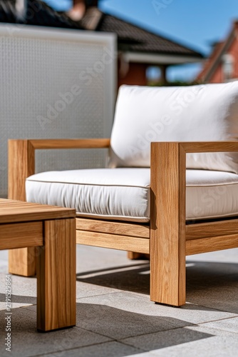 Teak patio chair with white cushions resting on stone terrace in bright daylight sharp focus shot for outdoor furniture marketing
