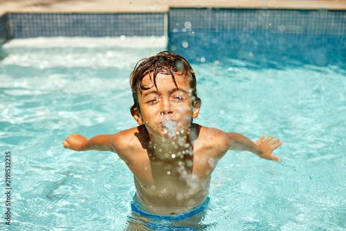 фотографія Boy, splash and excited in pool with playing, summer holiday and fun with break, energy and swimming