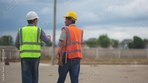 Construction engineers wearing hard hats and safety vests walking on a building site inspecting the project