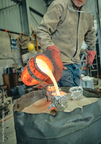 Obraz na płótnie A foundry worker pours intensely glowing molten metal from a heat-scorched cruci