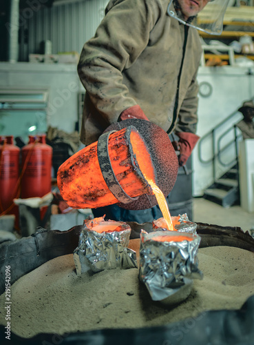Obraz na płótnie A foundry worker pours intensely glowing molten metal from a heat-scorched cruci