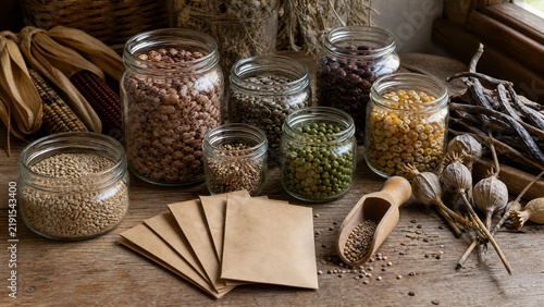 Assorted vegetable seeds in glass jars and paper envelopes on a rustic wooden table for gardening