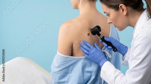 Healthcare worker evaluates a pigmented mole on a female patient wearing a hospital gown while using an illuminated magnifying glass in a bright office.