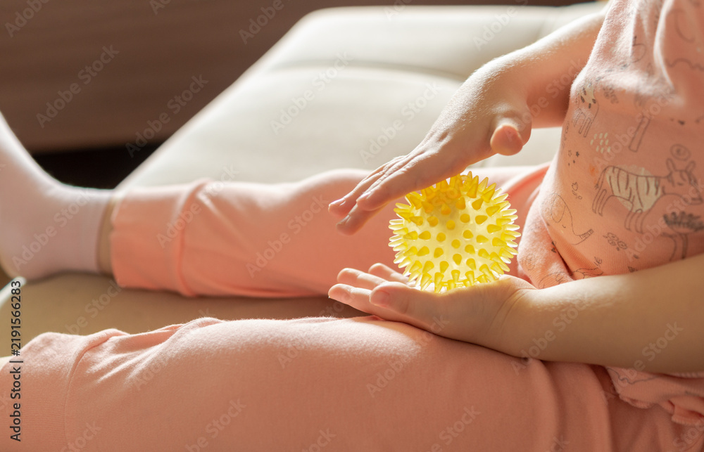 Obraz premium Unrecognizable child exploring a yellow spiky sensory massage ball at home. Tactile stimulation, sensory development, hand coordination and fine motor skills concept.