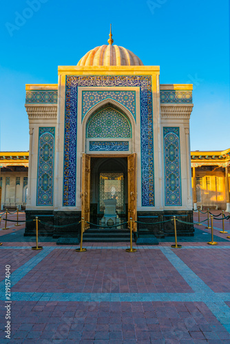 Front-facing view of the Islam Karimov Mausoleum in Samarkand, Uzbekistan, featuring a white ribbed dome, richly ornamented blue and turquoise tile-work, Arabic calligraphy, an arched entrance