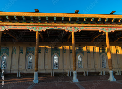 Long covered veranda of Hazrat Khizr Mosque in Samarkand, Uzbekistan, supported by carved wooden columns and decorated with a richly painted ceiling, ornamental floral friezes, pointed-arch windows