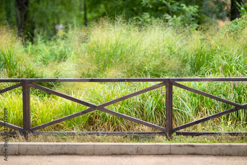 Canvastavla A sturdy dark brown wooden fence with geometric cross-beams fronts a paved path,