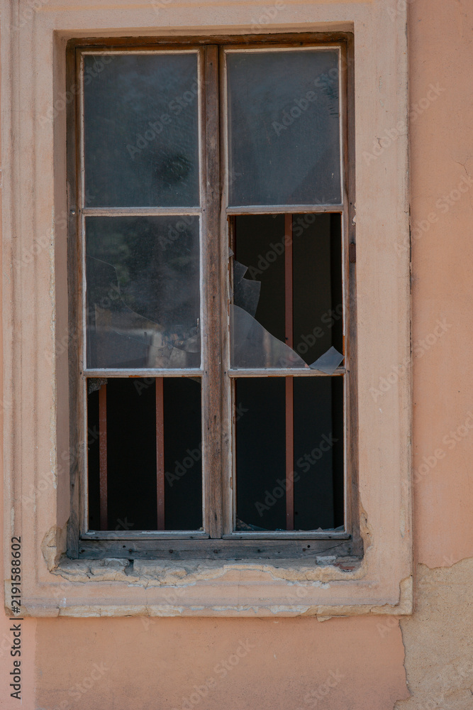 Fototapeta premium old broken window wooden frame cracked glass metal bars abandoned building beige wall weathered texture concept of urban decay, history, architecture