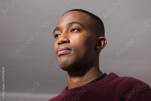African male posing for head-and-shoulders portrait in light-gray room, wearing burgundy sweater