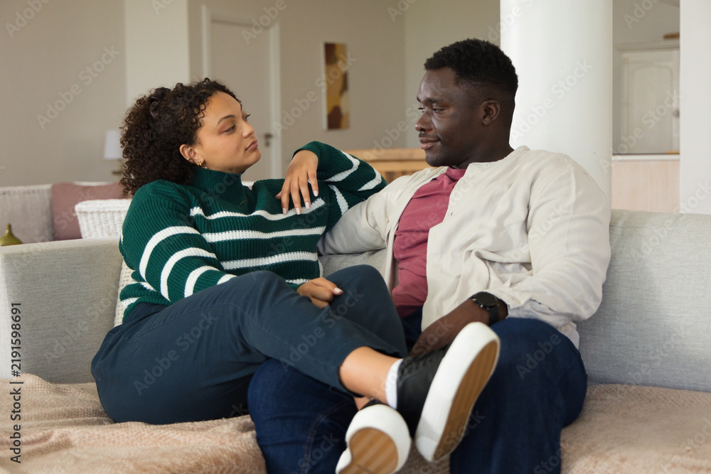 Obraz premium Couple sitting on sofa in living room, conversing while woman reclining wearing striped sweater