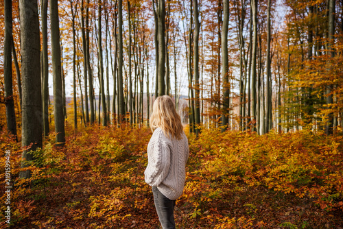 Woman in sweater stands in autumn woodland, relaxing and contemplating her thoughts. Forest bathing in fall season. Offline and digital detox concept